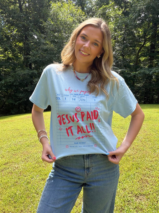 Rustic Rain Boutique light blue graphic t-shirt with red Jesus Paid It All text and bill design worn by a woman